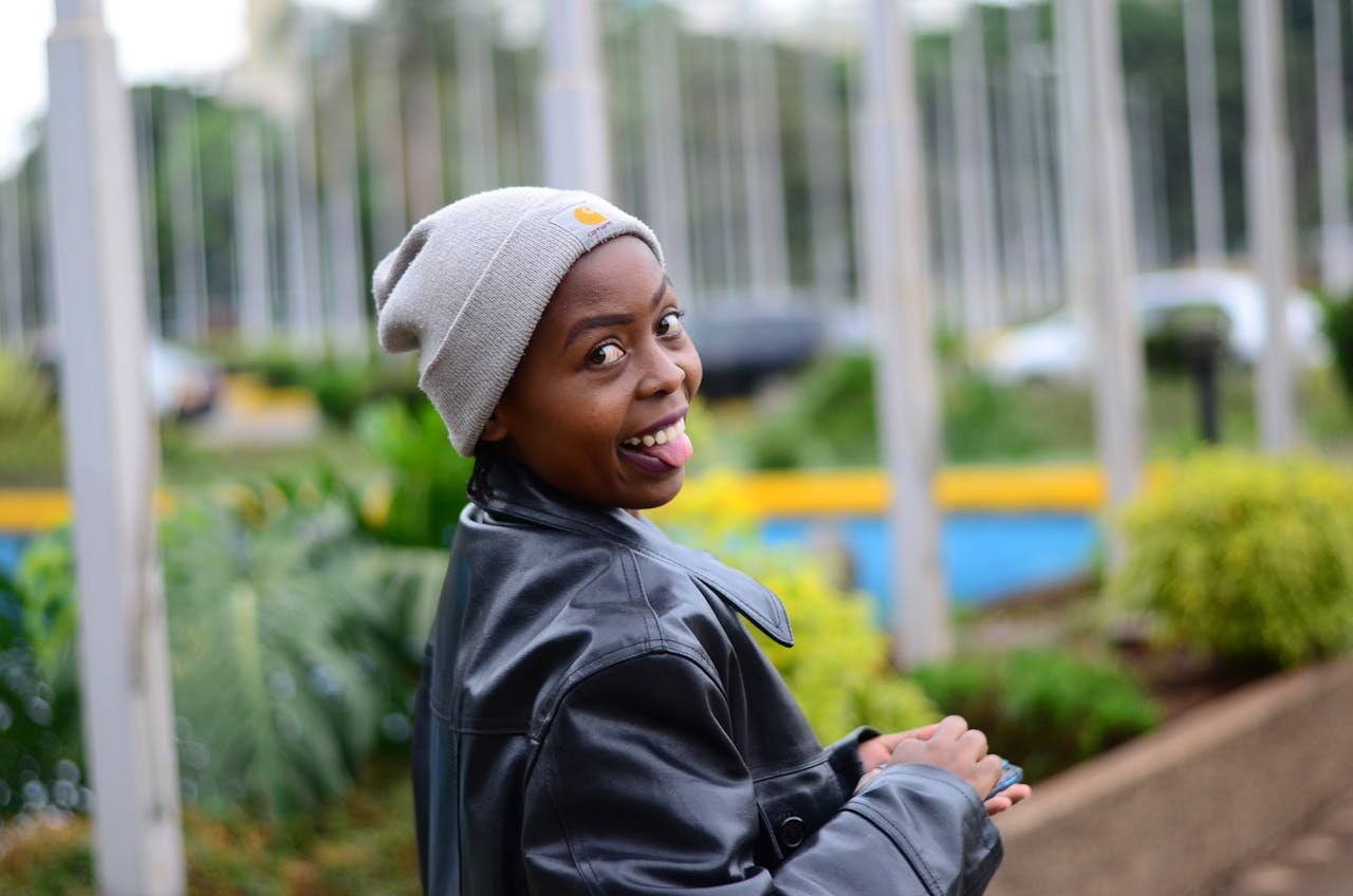 Smiling woman in a beanie and jacket with a playful expression outdoors in Nairobi.