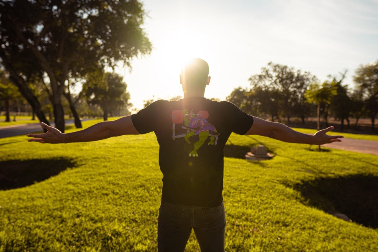Man in black shirt enjoying sunset in a lush green park. Symbolizes freedom.