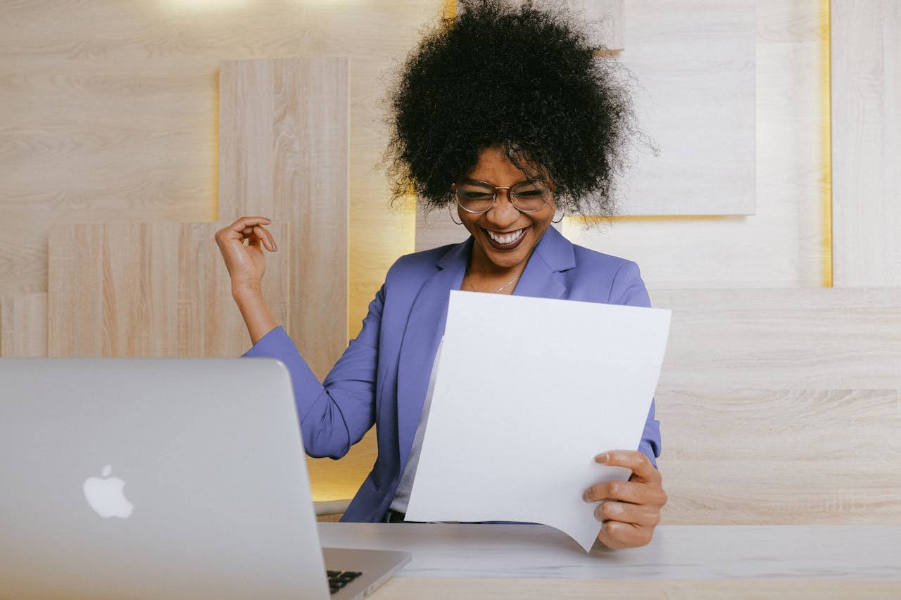 portfolio-03 A cheerful woman celebrates her success at work, looking at a document in an office setting.